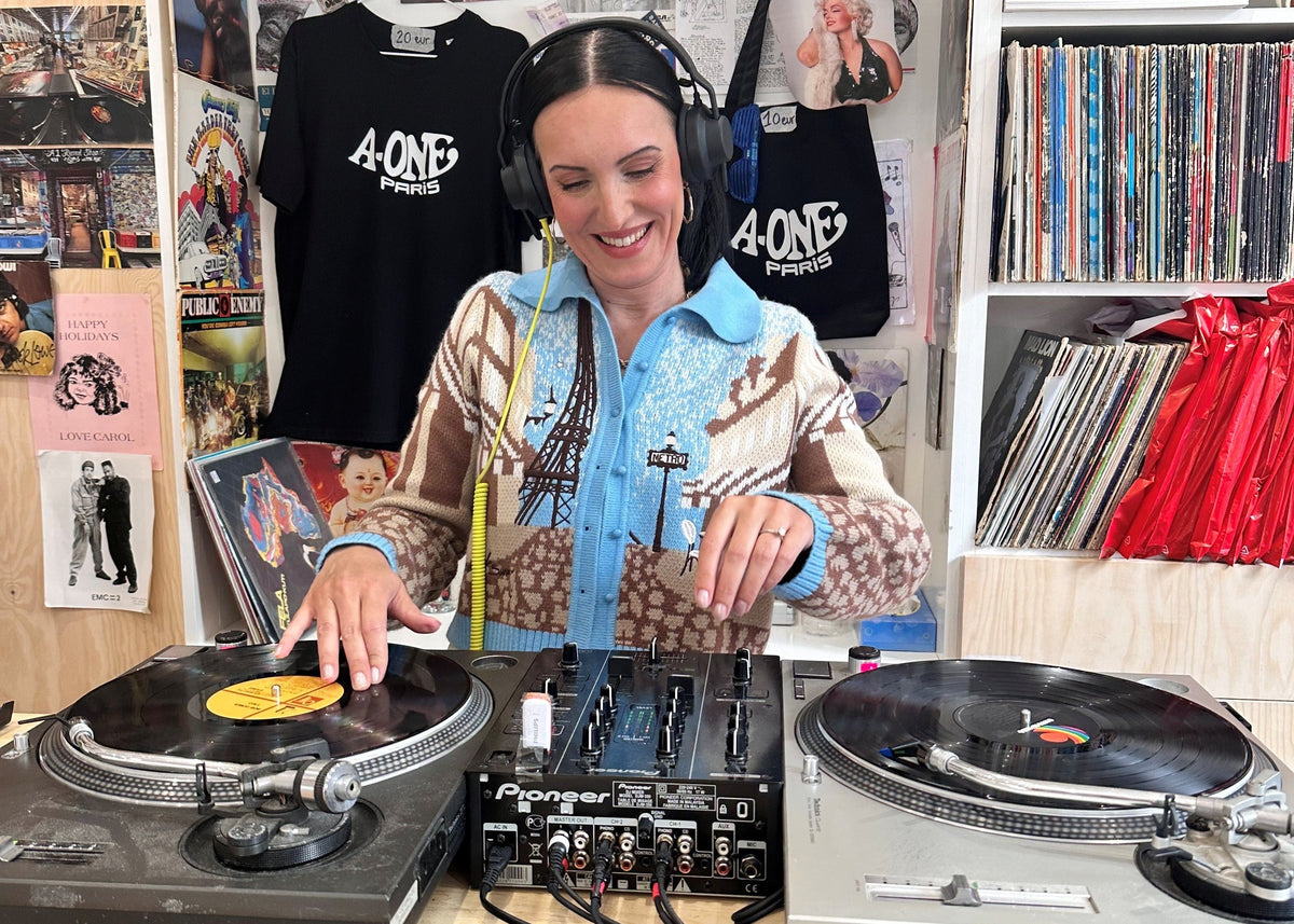 Tia DJing in a room with vinyl records and music equipment.